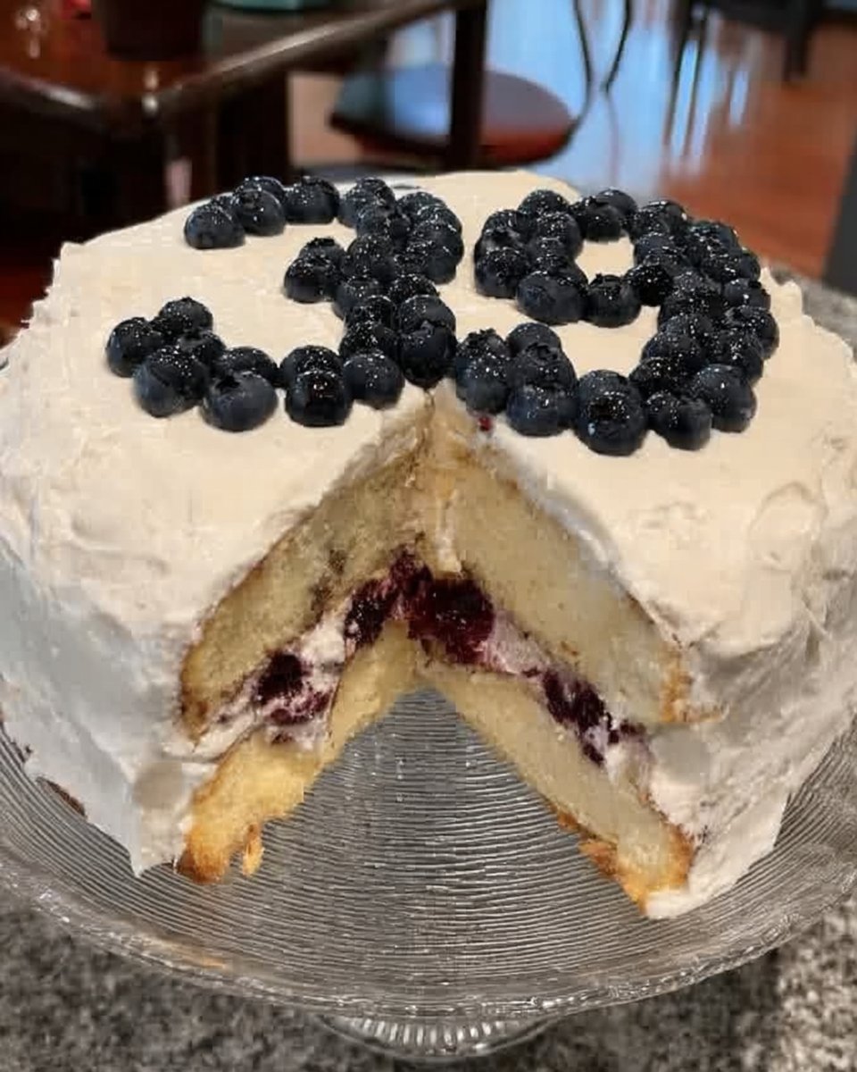 Lemon Blueberry Cake 13 Hands spreading lemon buttercream on a cake layer