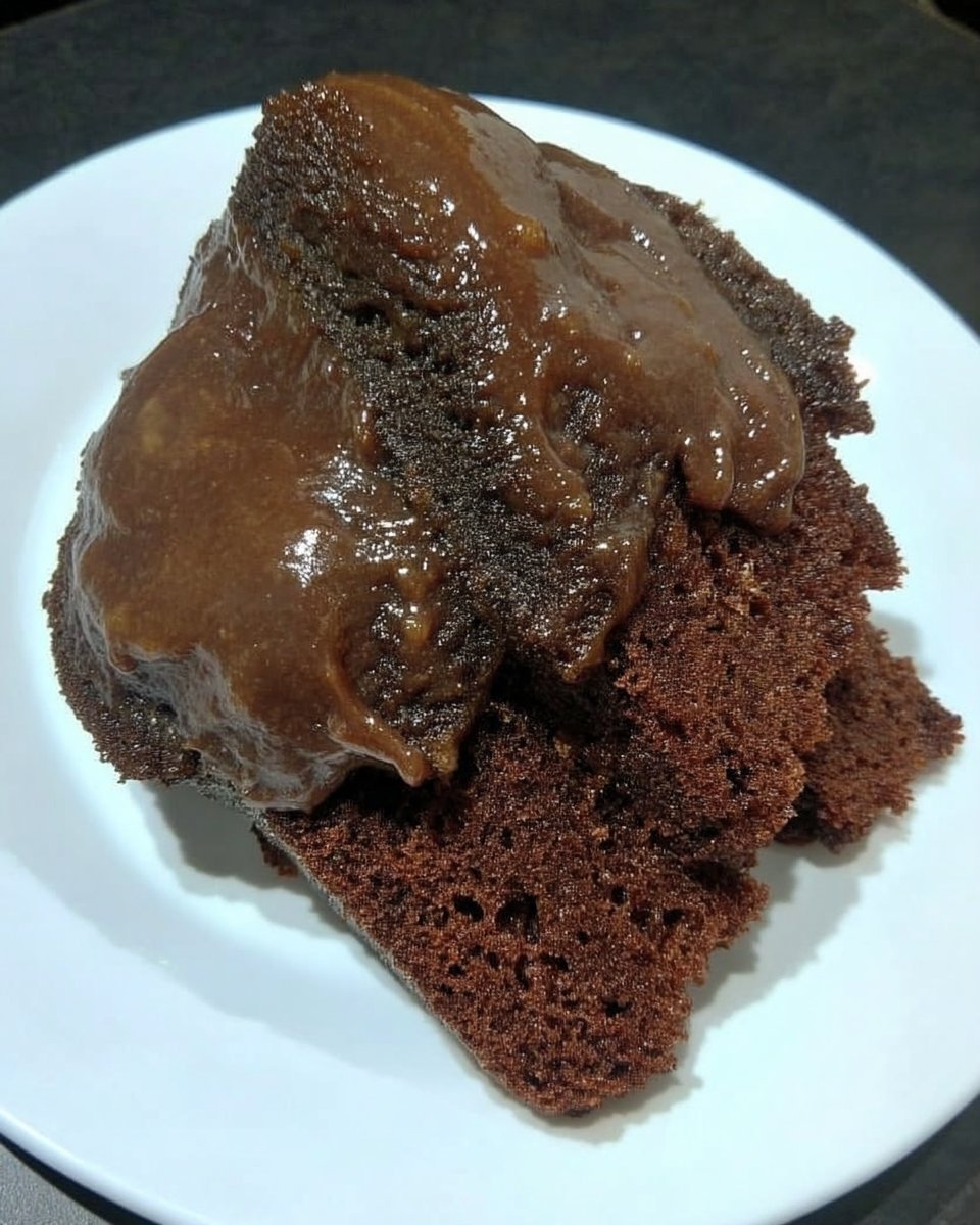 Slice of dense chocolate fudge cake with glossy glaze on a ceramic plate