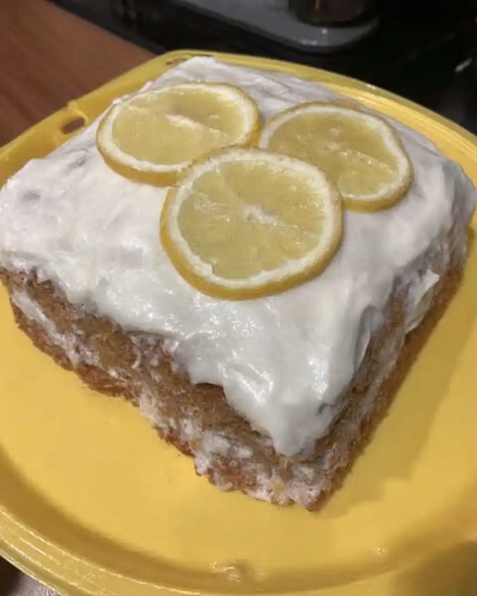 Slice of moist lemon layer cake on a floral plate next to a cup of tea