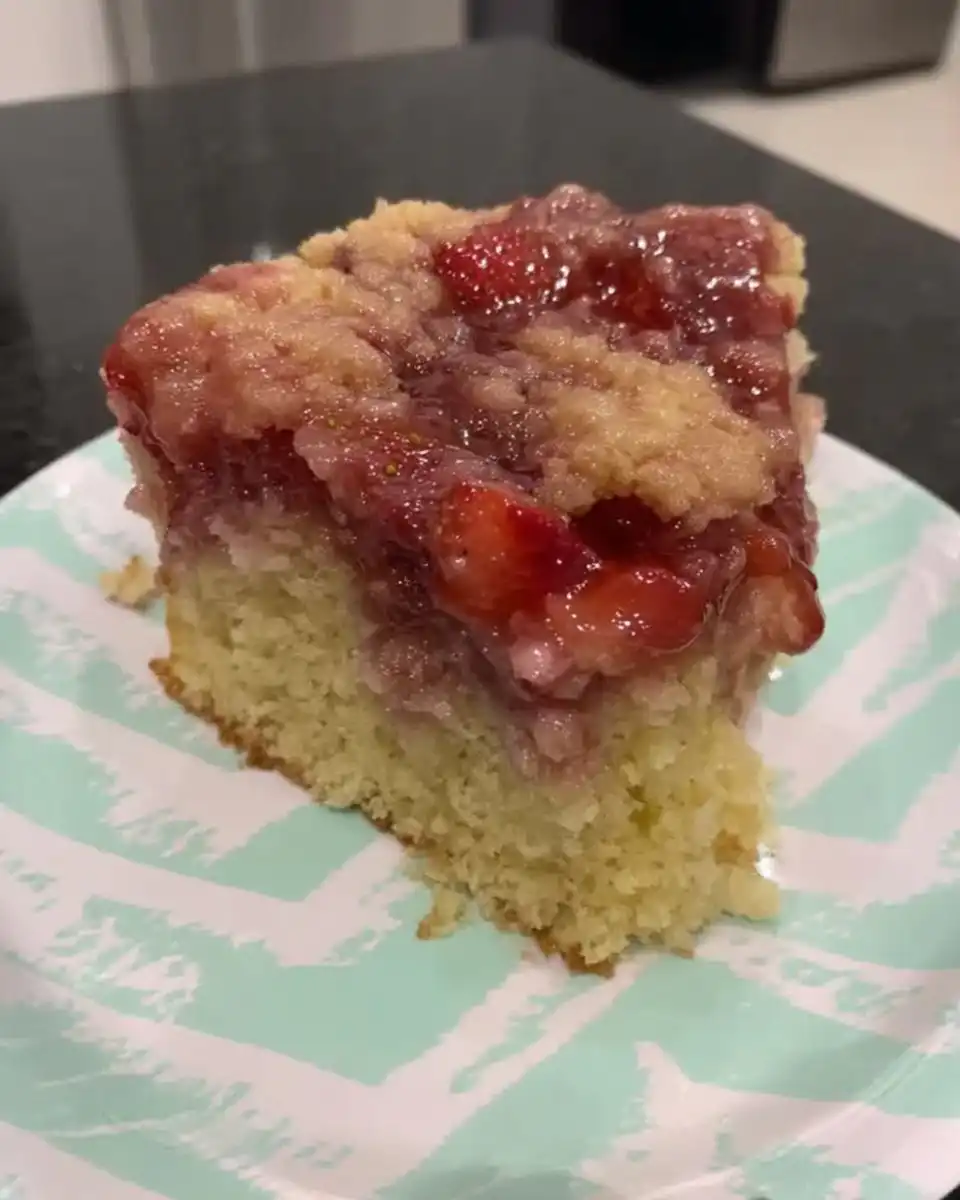 Square of strawberry rhubarb cake dusted with powdered sugar next to coffee