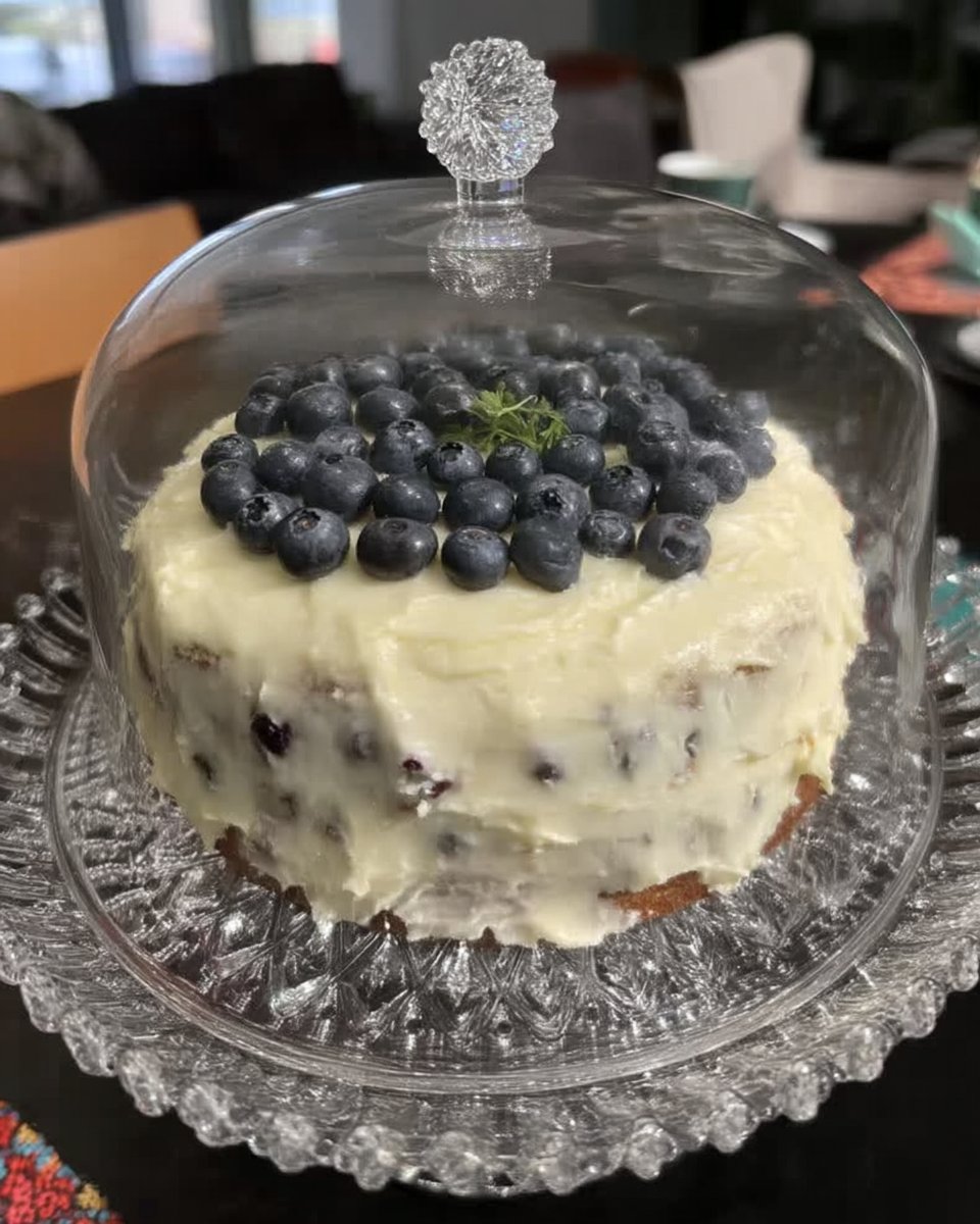 Whole vintage lemon blueberry cake on a ceramic cake stand with fresh lemons nearby
