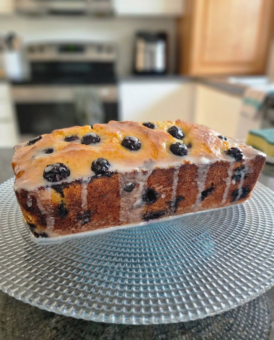 A slice of lemon blueberry cake on a small saucer next to a cup of tea.