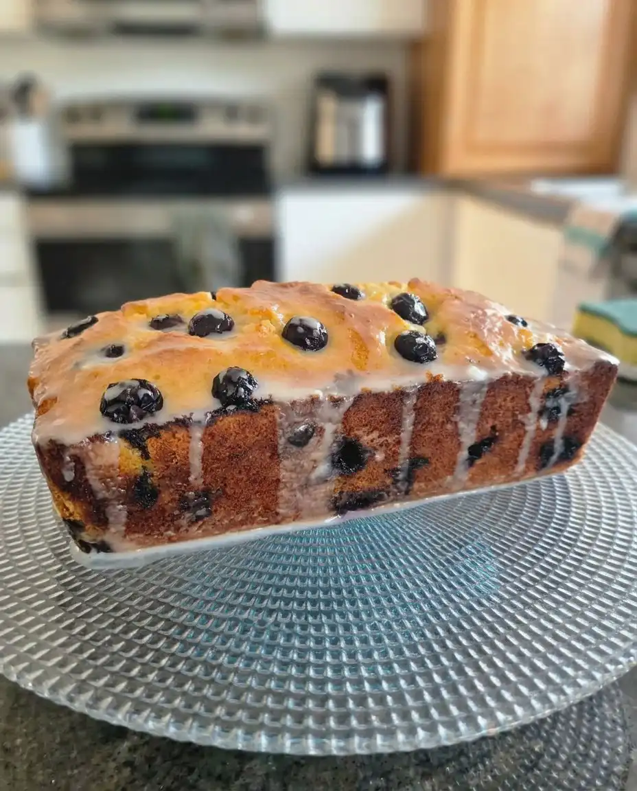 A slice of lemon blueberry cake on a small saucer next to a cup of tea.