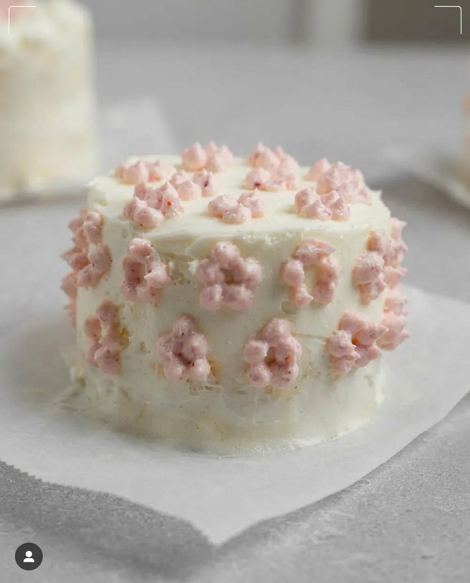 A small vanilla cake with purple decorations nestled inside a white clamshell container