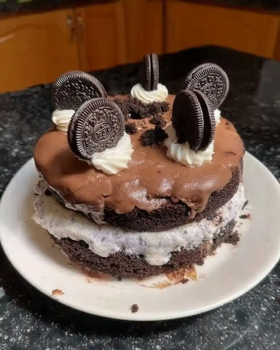 A single slice of Oreo cake on a white plate showing distinct layers of frosting and ganache