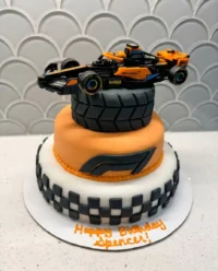 A completed F1 cake with bright orange icing and liquorice tires on a racing track board