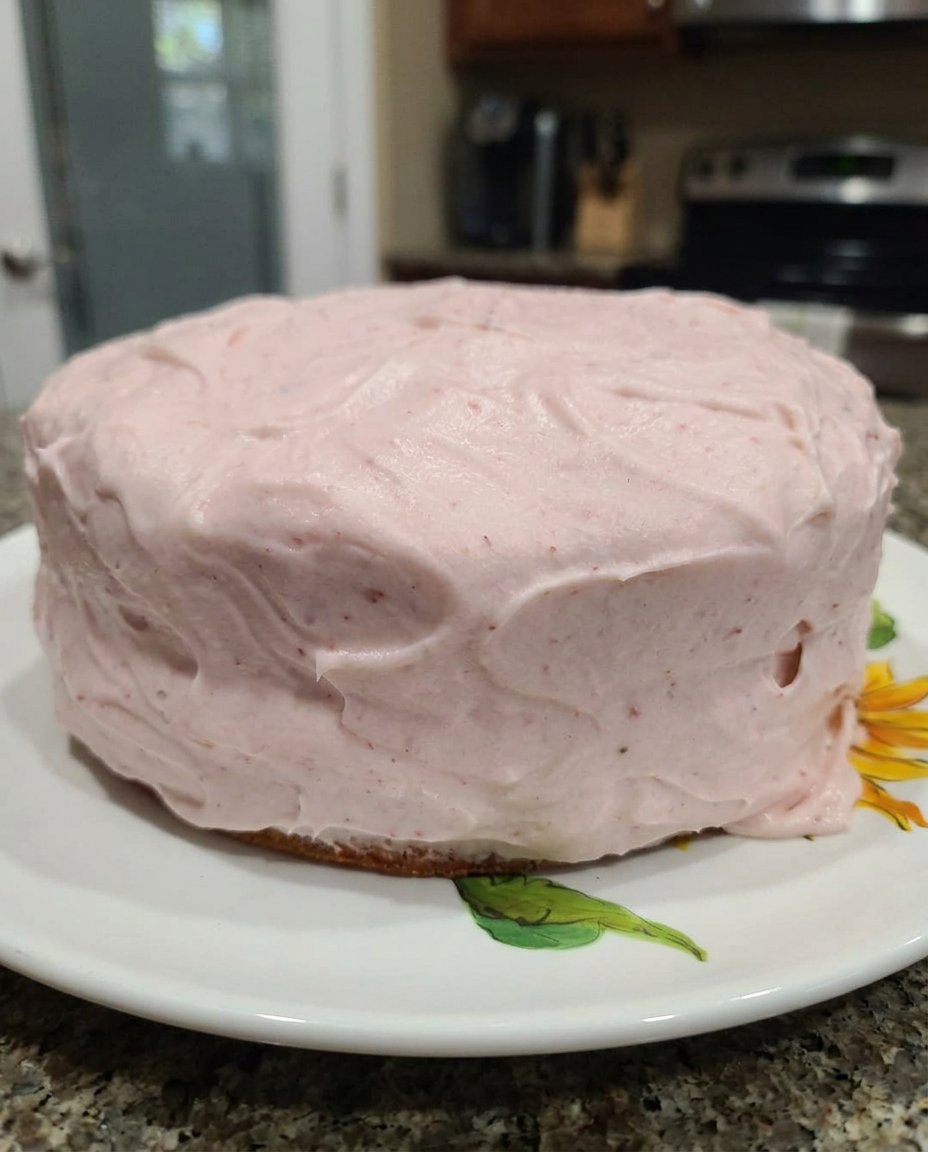 A slice of fresh strawberry cake with pink frosting on a vintage floral plate