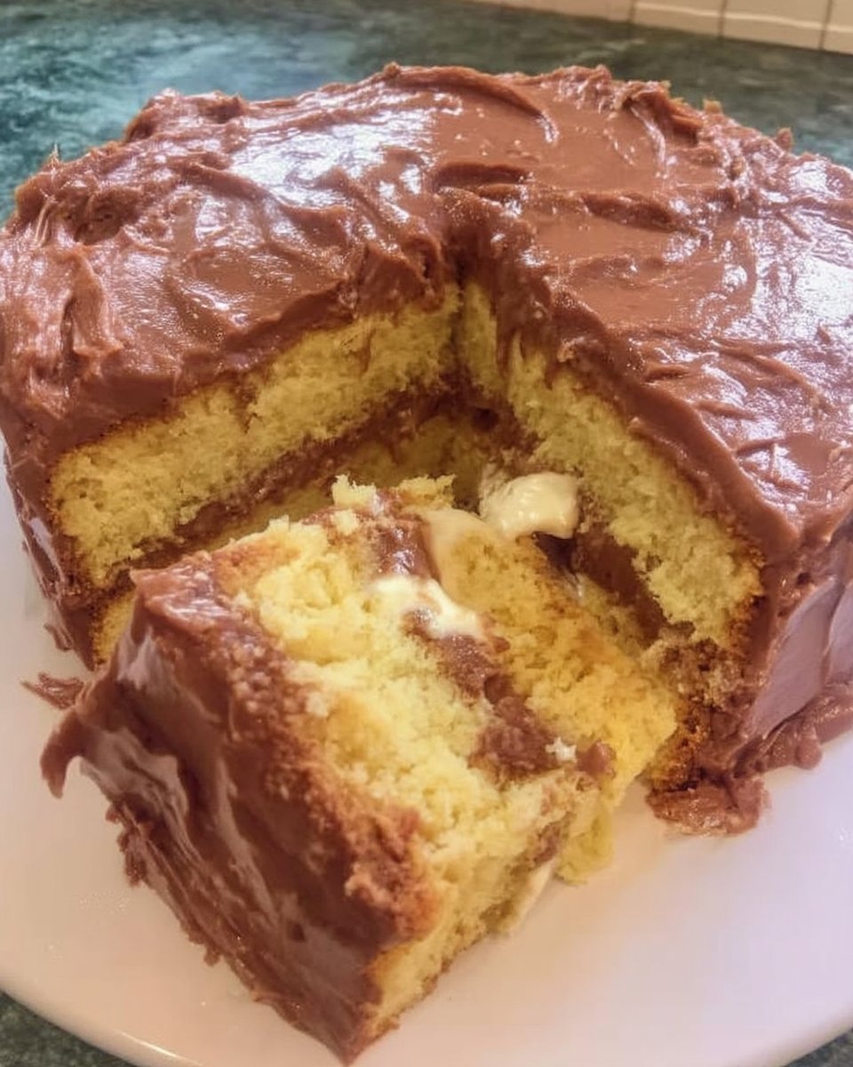 A single slice of yellow cake with chocolate buttercream on a white plate