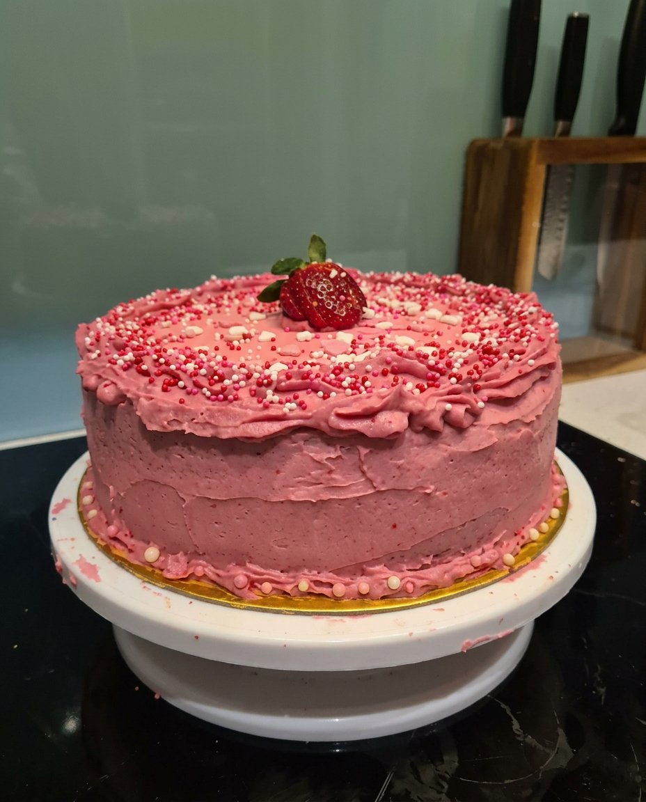 A thick slice of strawberry cake topped with a dollop of whipped cream and a dusting of sugar.