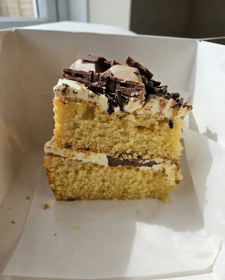 A hand using an offset spatula to spread cream cheese frosting over a cooled cake