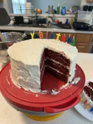 A close up shot of a sliced red cake with thick cream cheese frosting and pecan garnish