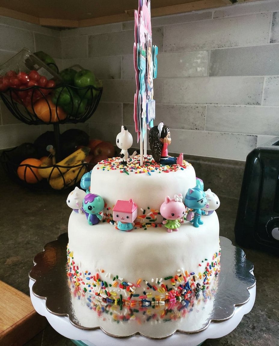 A two-layer vanilla cake with pink frosting and colorful sprinkles on a vintage plate