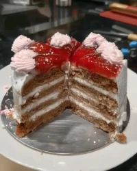 A two-layer fresh strawberry cake with pink buttercream frosting on a vintage glass pedestal