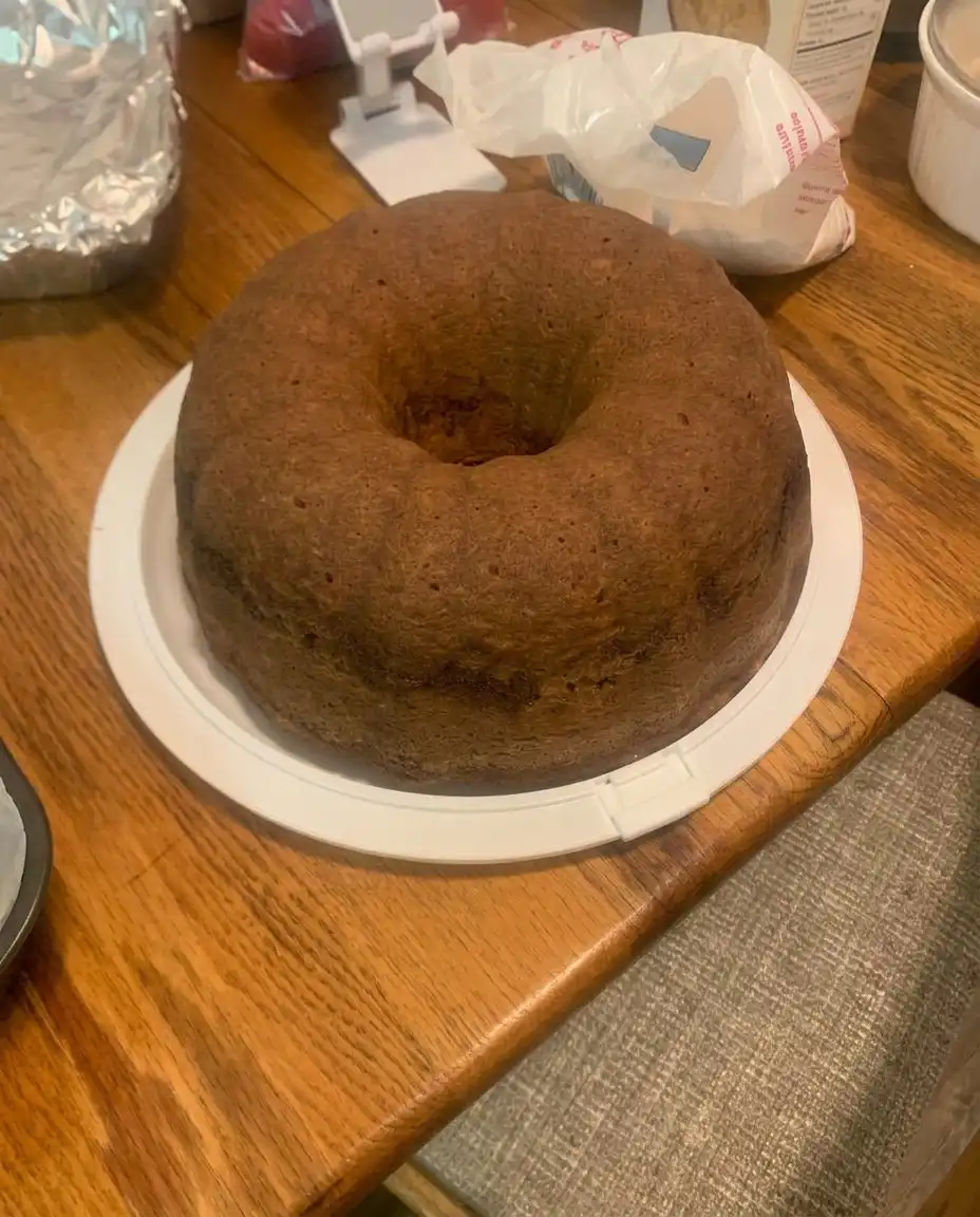 A hand dusting a bundt pan with flour over a wooden counter.