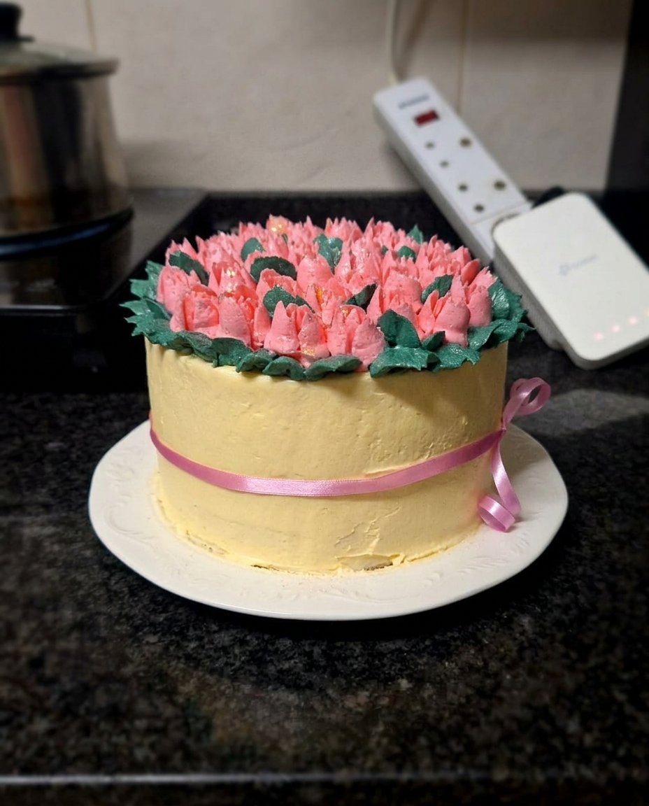 A 6-inch ivory cake decorated with piped buttercream tulips in burgundy and purple resting on a chrome cooling rack