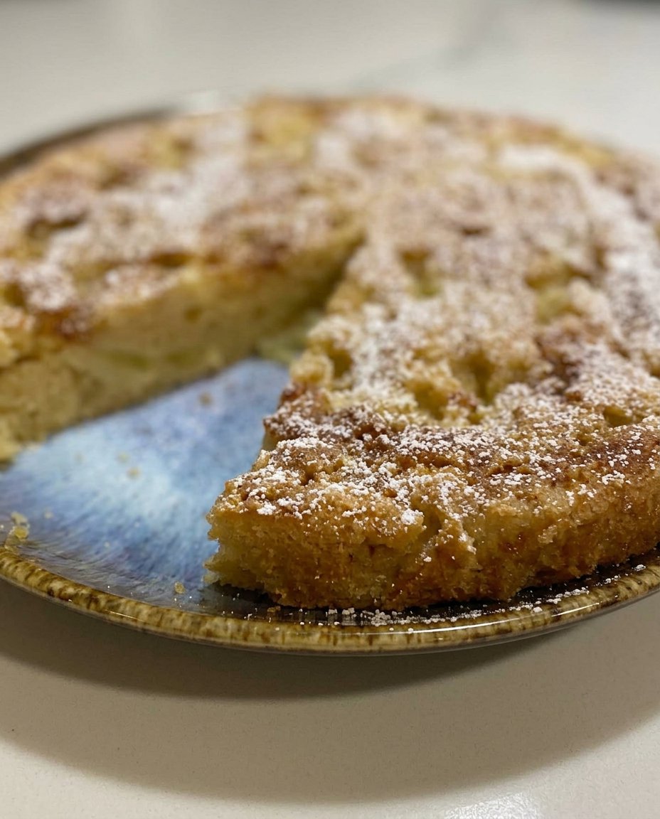 A single slice of moist apple cake showing visible fruit pieces on a white porcelain plate