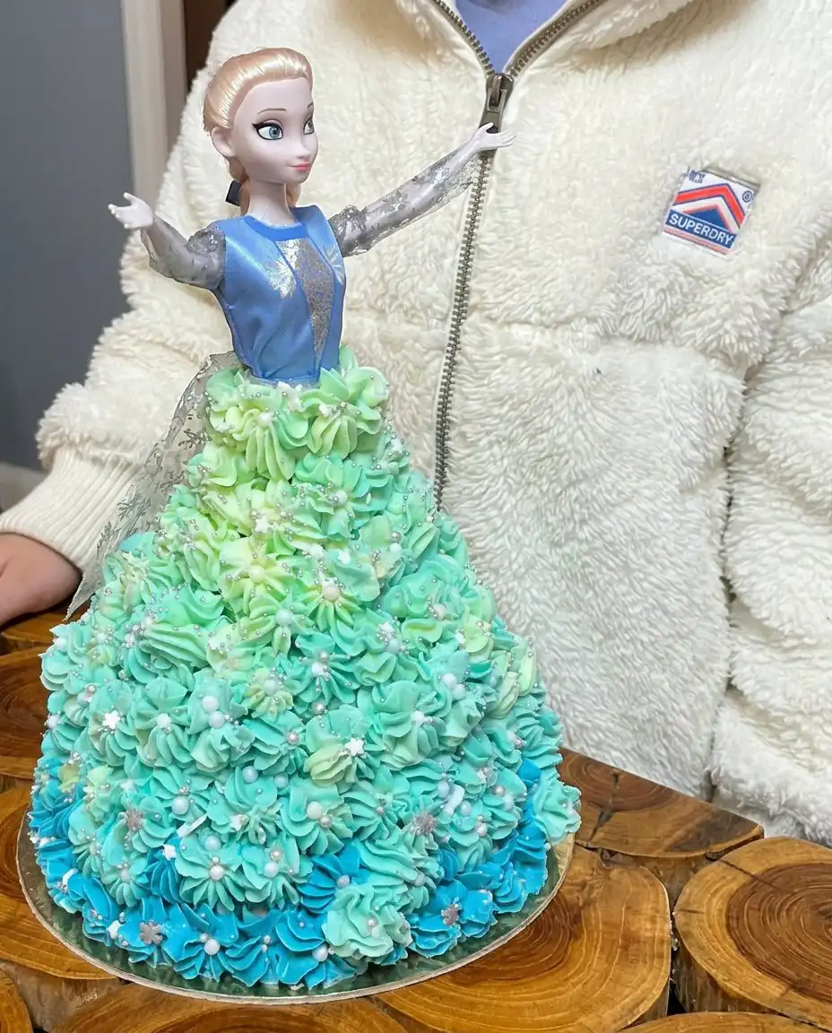 Elsa Cake 10 A tall Elsa cake shaped like a dress with blue icing and silver sprinkles.