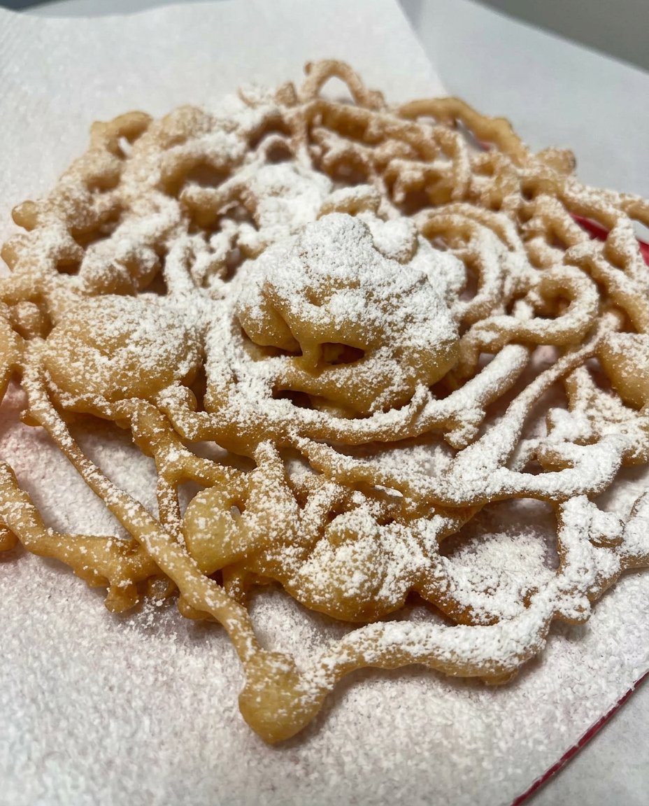 Funnel cake piled high with powdered sugar on a decorative plate