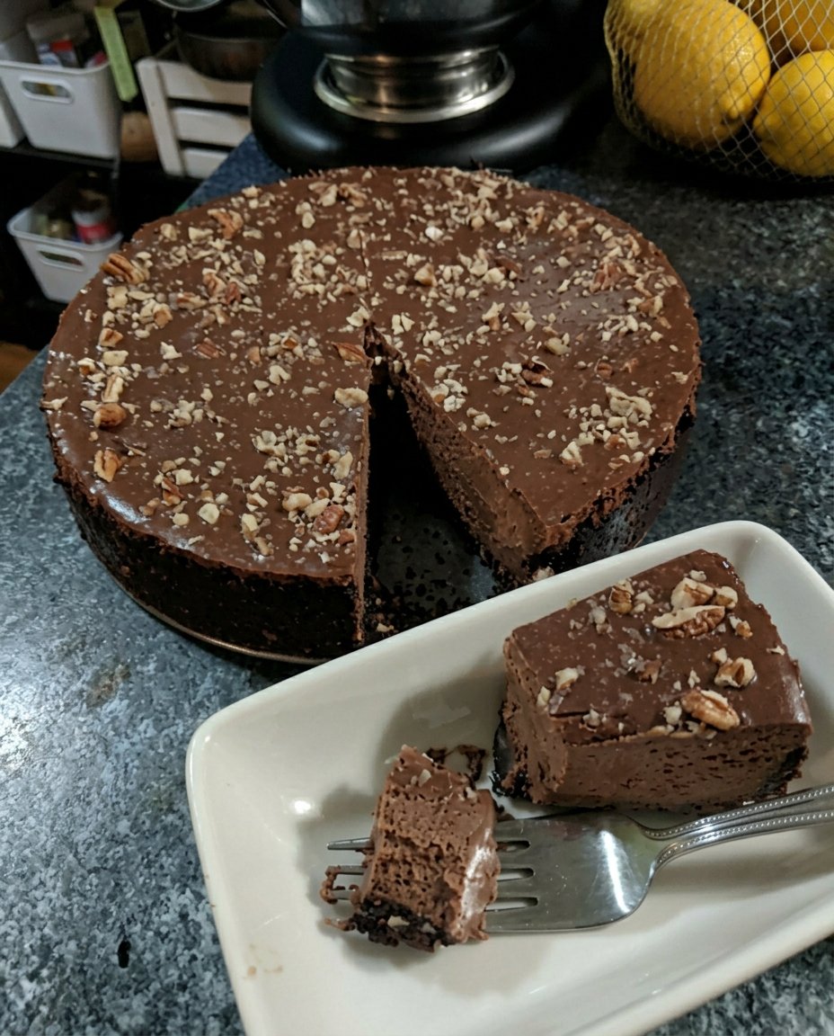 A finished chocolate truffle cake with a glossy glaze on a silver cake stand