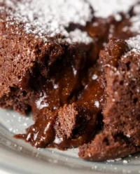 A close up shot of a chocolate lava cake with a molten center flowing onto a white plate