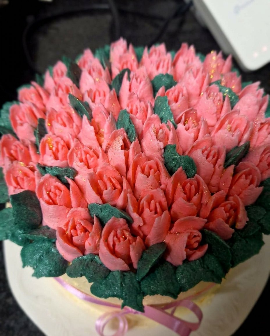 A slice of vanilla cake with ivory icing and a piped tulip on a vintage china plate
