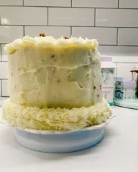 A pink multi layered cake being assembled with strawberry frosting and raspberry sponges