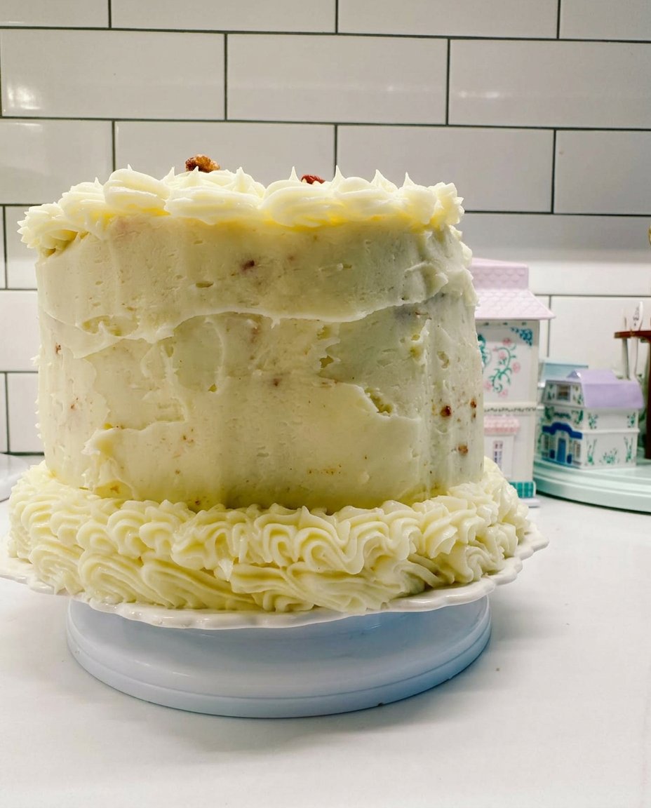 A pink multi layered cake being assembled with strawberry frosting and raspberry sponges