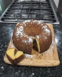 A golden brown Sock It To Me Cake with a white glaze on a vintage floral plate.