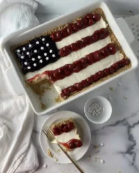A stunning no-bake American flag cheesecake with a vibrant red, white, and blue fruit topping.