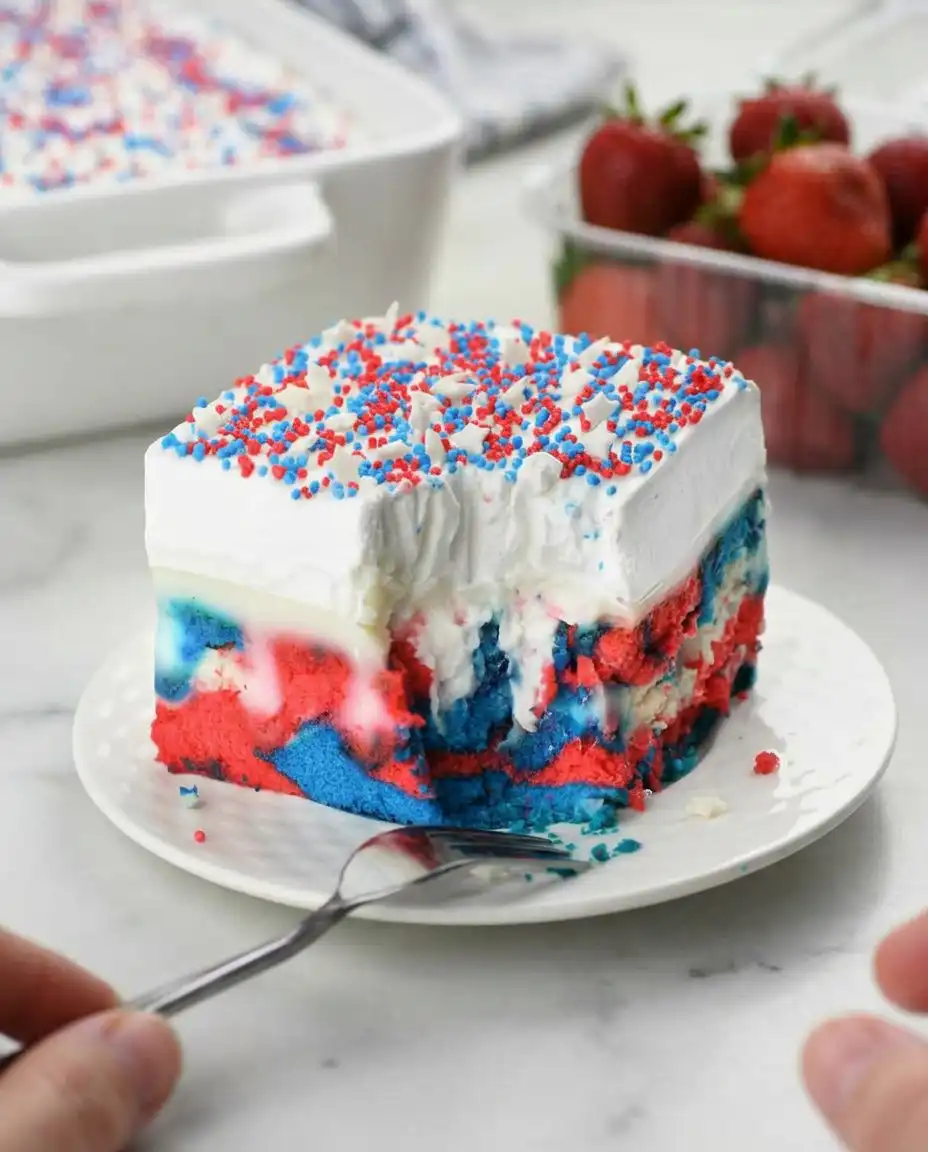 A chilled slice of patriotic poke cake served on a summer porch next to a glass of lemonade
