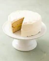 A beautiful Classic Vanilla Bean Layer Cake sits on a rustic wooden table with vanilla beans.