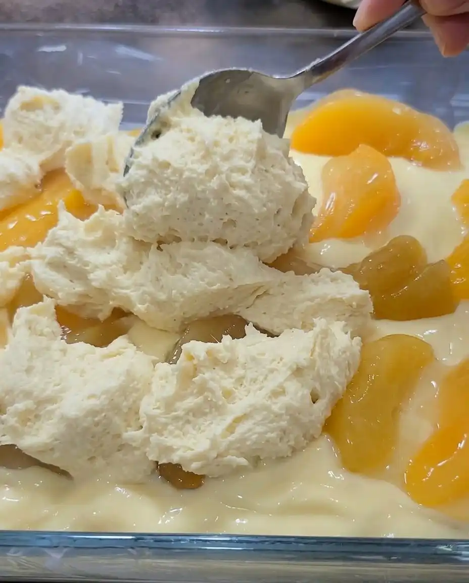 A hand drizzling white almond glaze over a pan of baked Peaches and Cream Bars.