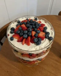 Tall glass trifle dish filled with precise layers of angel food cake, white chocolate pudding, and fresh summer berries.