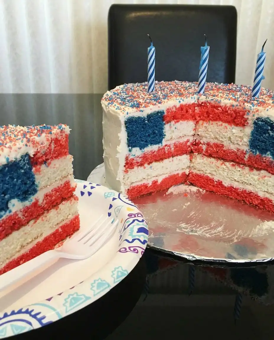 A whole white frosted cake on a pedestal stand decorated with red white and blue sprinkles.