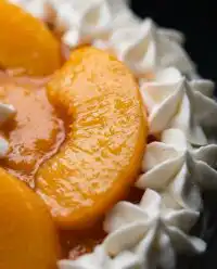 A tall three layer Peaches and Cream Layer Cake with vanilla bean whipped cream and fresh peach slices.