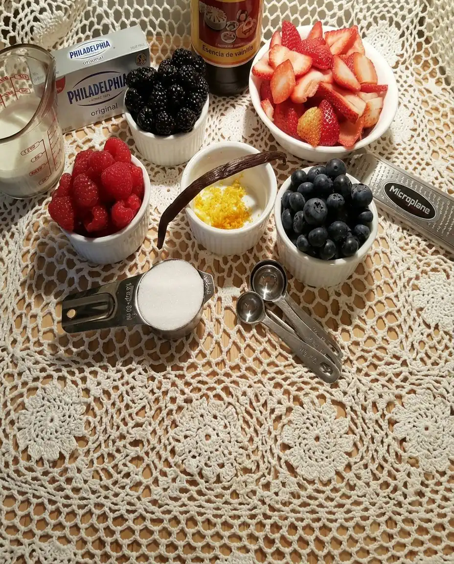 Fresh strawberries, blueberries, cream cheese, and mini marshmallows arranged on a wooden kitchen table.