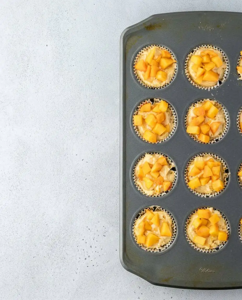 Close up of a muffin top with peach chunks and buttery crumbles
