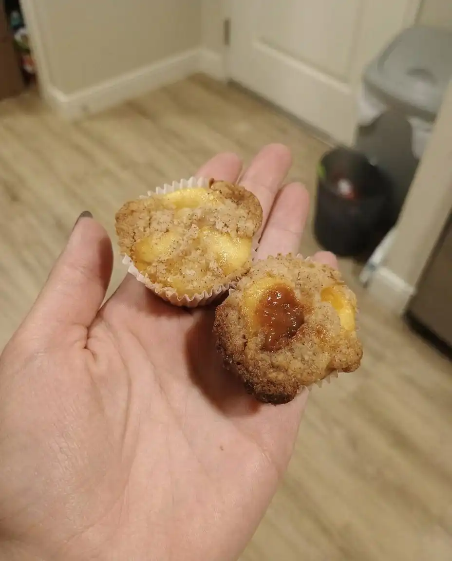 A hand using a wooden spoon to stir peach muffin batter in a white bowl