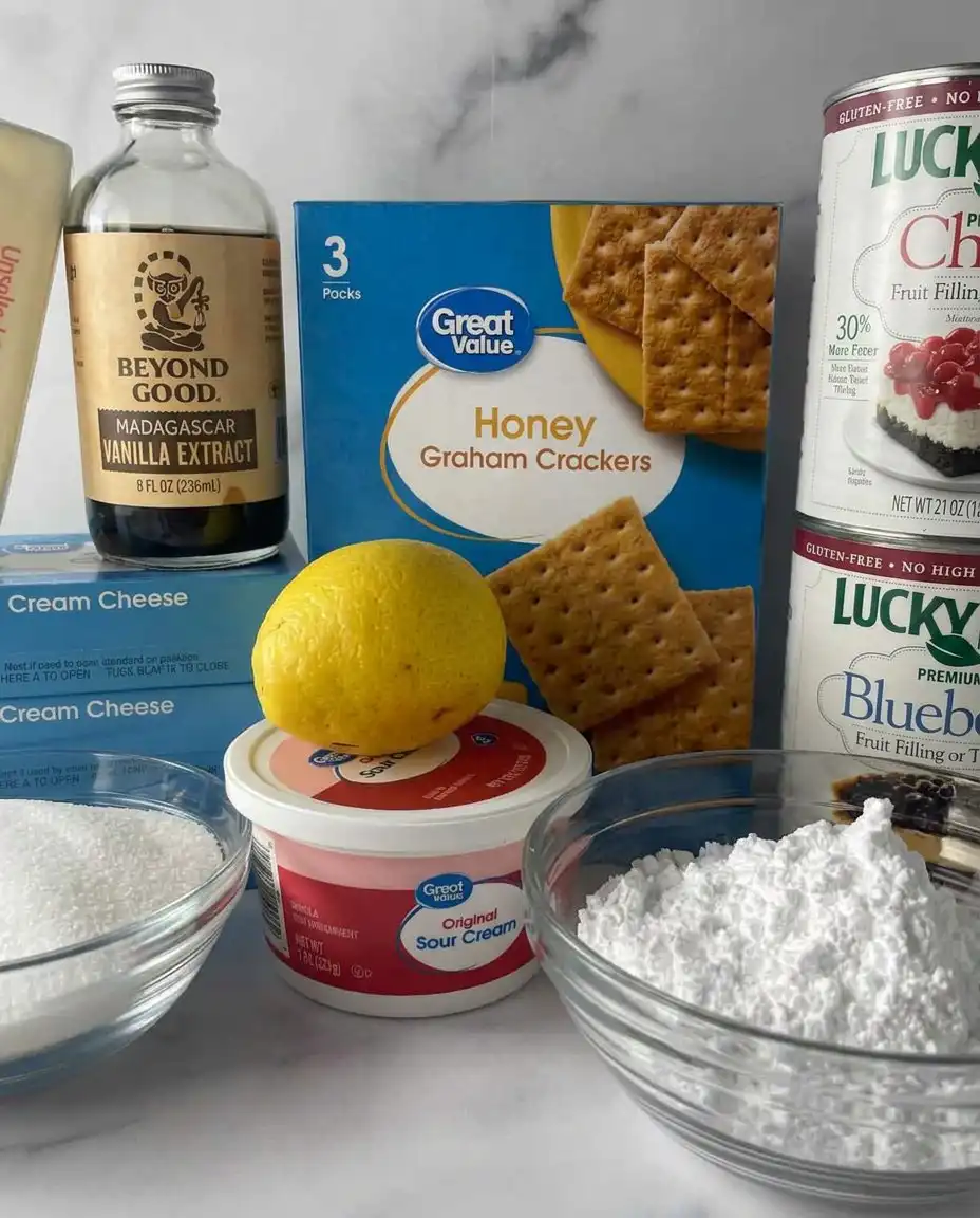 Overhead view of graham cracker crumbs, cream cheese, heavy cream, and fruit fillings for no-bake cheesecake.