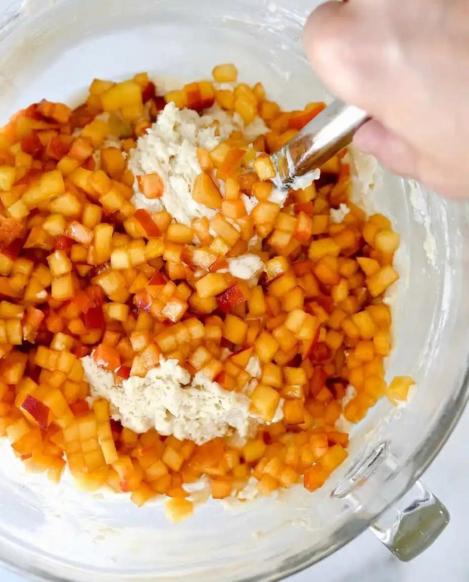 Bowls of flour, honey, peach preserves, and fresh peaches on a wooden counter