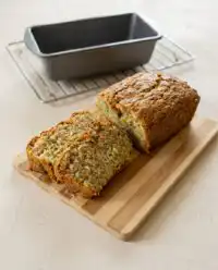 A moist Lemon Zucchini Cake loaf cooling on parchment paper with fresh citrus zest.