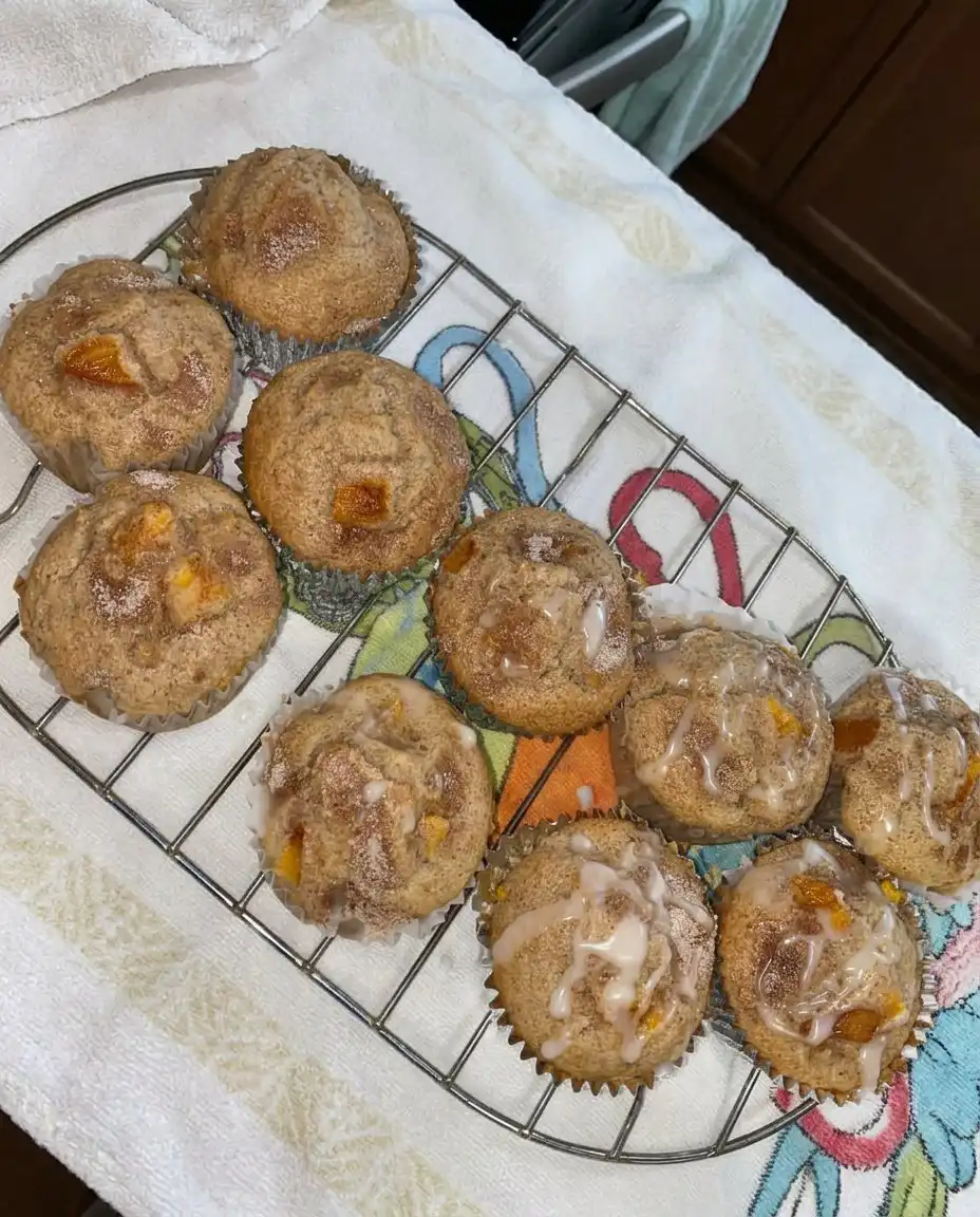 A peach cobbler muffin on a floral china plate next to a cup of tea