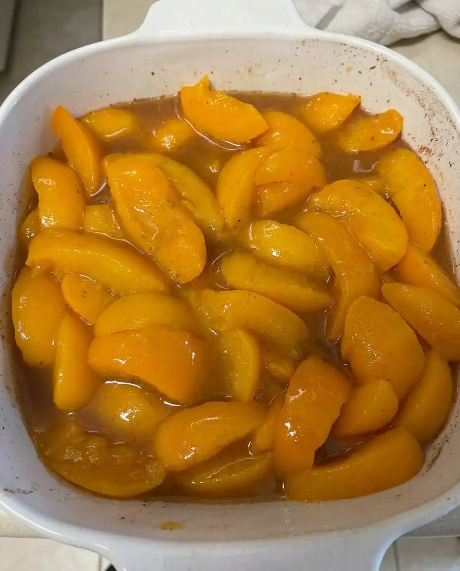 Cans of peach pie filling, a box of vanilla cake mix, and a stick of butter on a wooden kitchen counter.