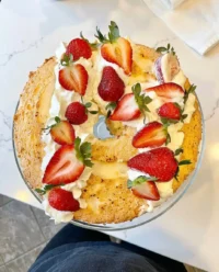 A towering angel food cake layered with thick coconut whipped cream and overflowing with fresh strawberries and blueberries.