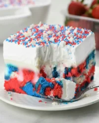 Slice of red, white, and blue patriotic poke cake on a vintage white plate