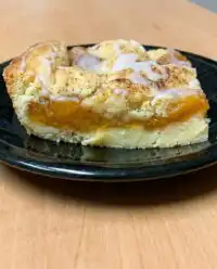 A freshly baked Peach Coffee Cake sitting on a rustic wooden table in a sunlit kitchen.