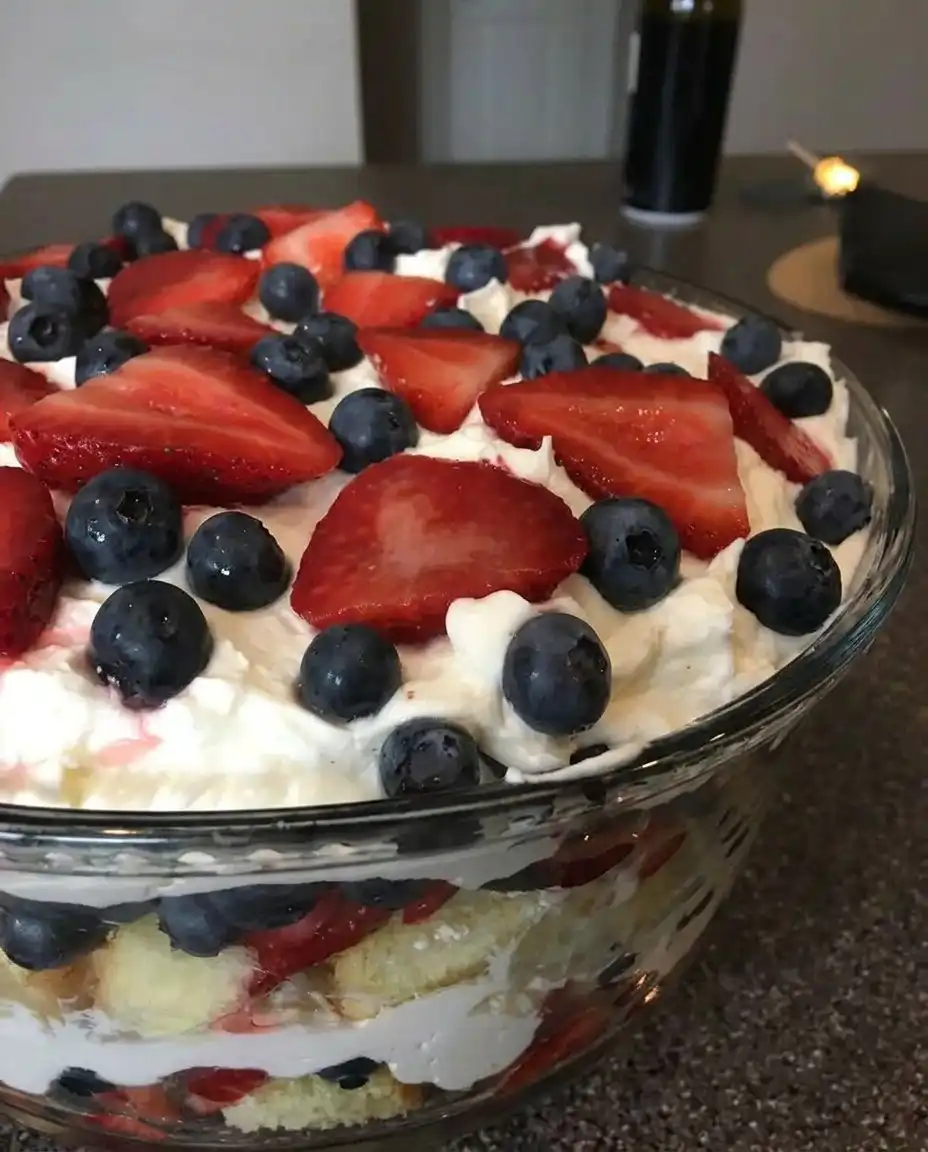 A baker carefully arranging sliced strawberries against the glass of a trifle bowl.