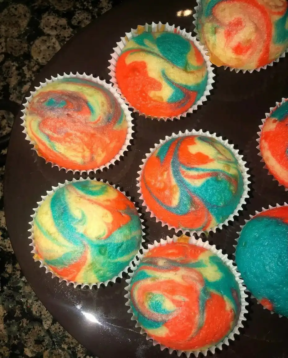 A hand piping a blue and white buttercream rosette onto a chocolate cupcake