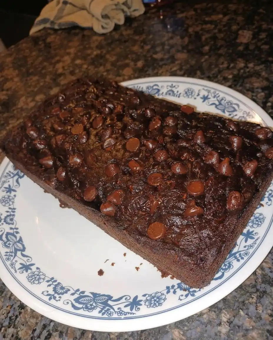 A slice of chocolate zucchini bread on a white plate with cream