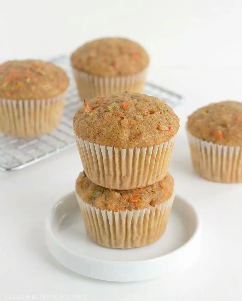 Two zucchini carrot oatmeal muffins served on a white plate next to a cup of hot tea.